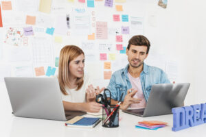 smiling male female sitting desk talking looking laptop scaled